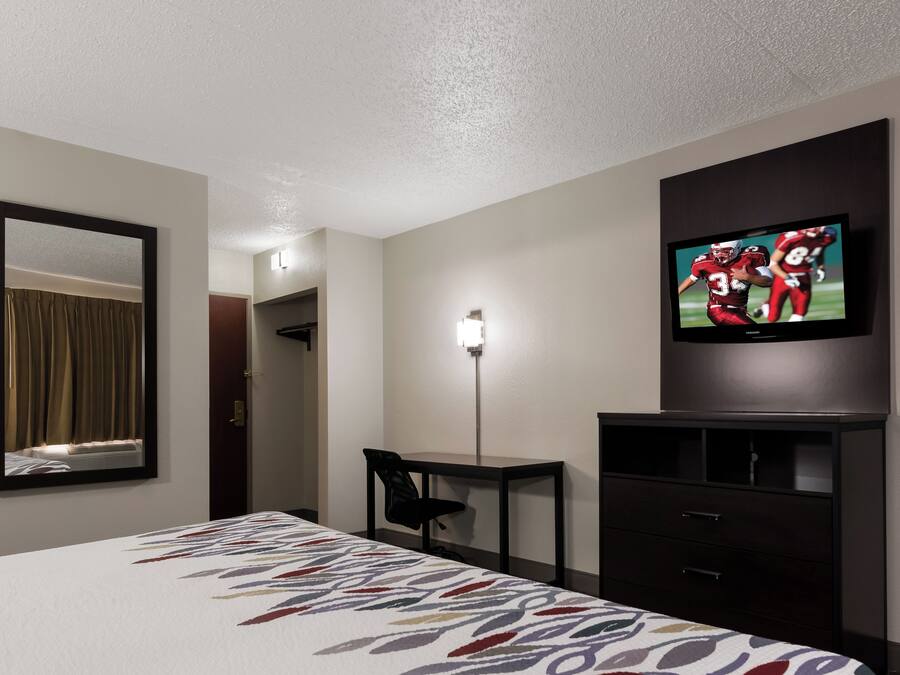 Habitación de hotel con cama, escritorio, silla, televisor y espejo.