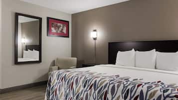 Ein Hotelzimmer mit einem großen Bett, einem Sessel, einem Nachttisch, einem wandmontierten Spiegel und einem gerahmten Bild.