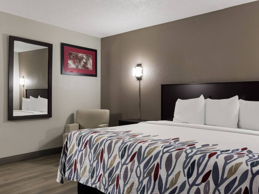 A hotel room with a large bed, a chair, a nightstand, a wall-mounted mirror, and a framed picture.