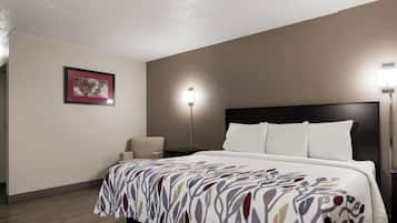 A hotel room with a bed, a chair, a nightstand, a lamp, and a framed picture on the wall.