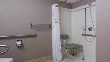 Un baño con inodoro, ducha con barra de apoyo, banco accesible para sillas de ruedas y secador de manos.