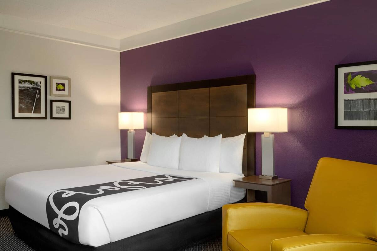 Una habitación de hotel con una cama grande, dos lámparas de noche, un cabecero y un sillón amarillo.