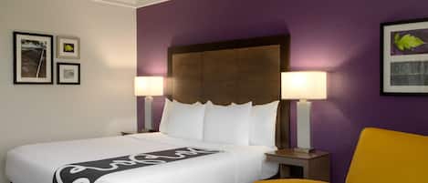 Une chambre d’hôtel avec un grand lit, deux lampes de chevet, une tête de lit et un fauteuil jaune.