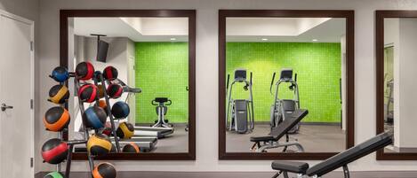 Een sportschool met trainingsapparatuur, spiegels en een groene wand.