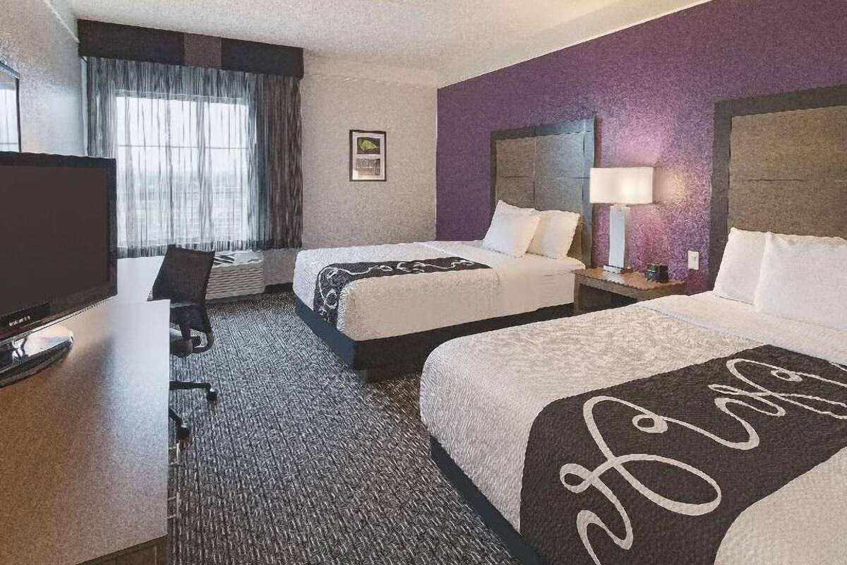 Habitación de hotel con dos camas, televisión, escritorio y ventana con cortinas.