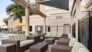 Un área de estar techada al aire libre con mobiliario de mimbre y una piscina al fondo.