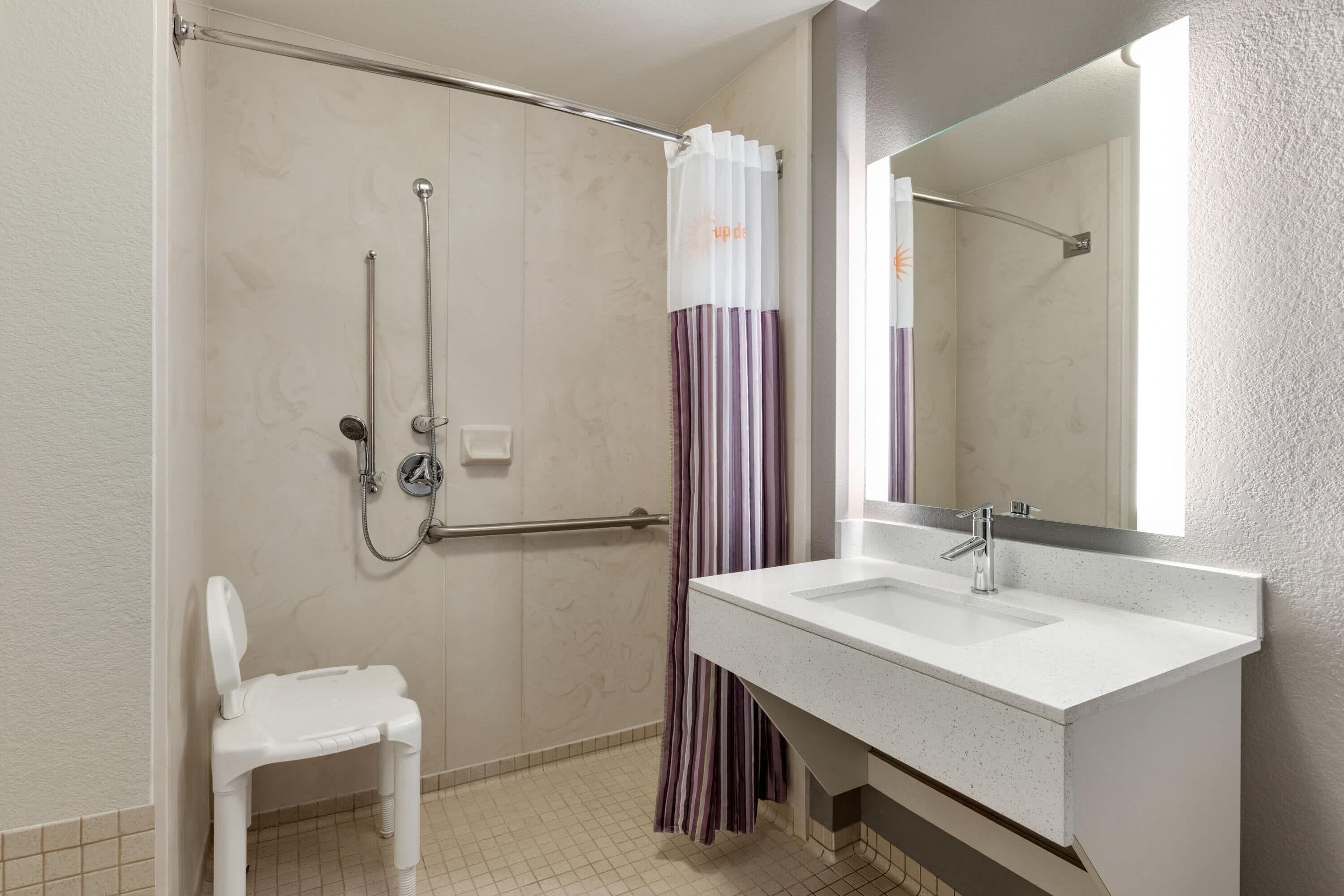 A bathroom with a white sink, a mirror, a shower with a handrail, and a white toilet.
