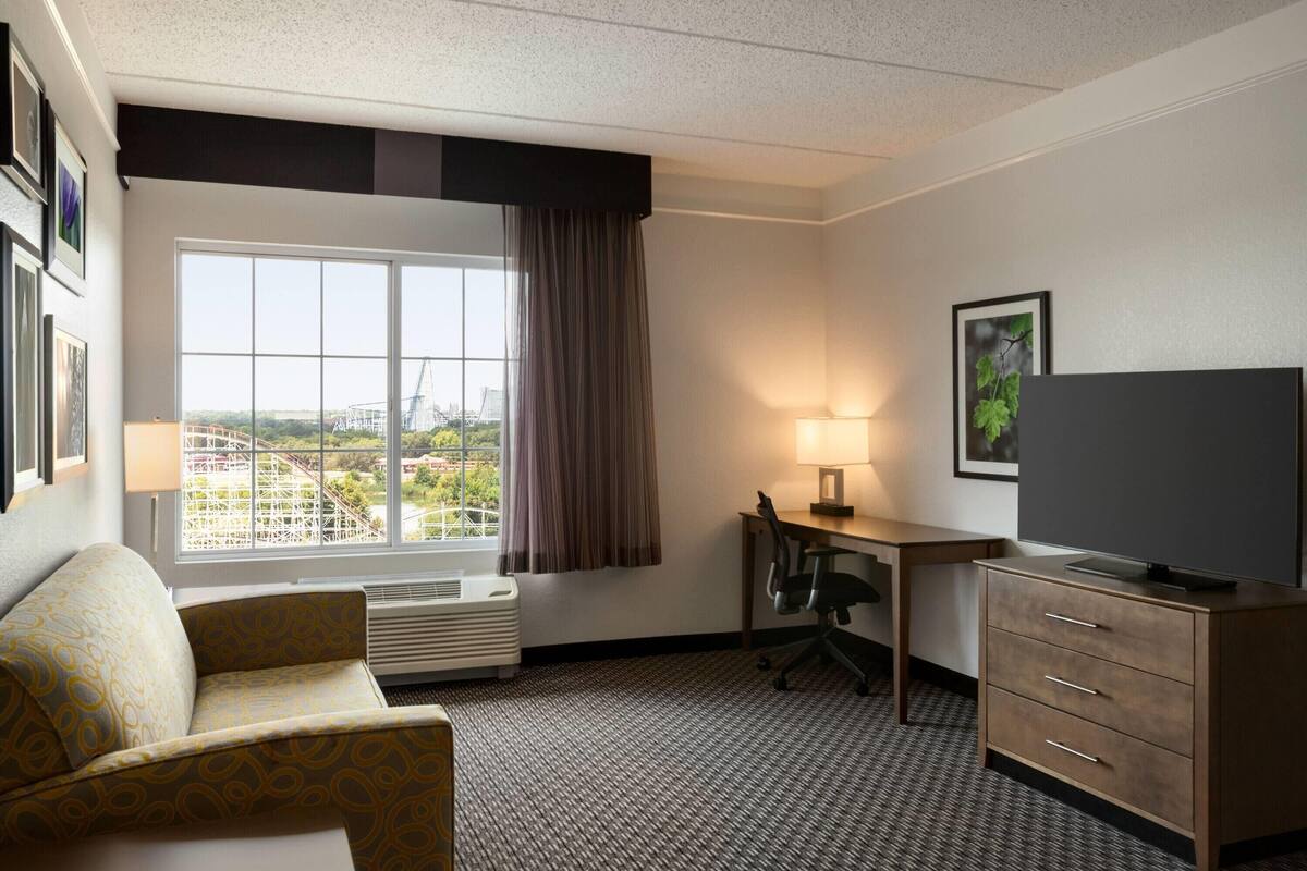 Habitación de hotel con un ventanal grande, un escritorio, una silla, un televisor y una cama.