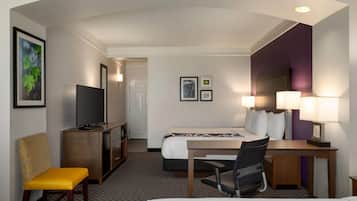 A hotel room with a bed, desk, chair, TV, and a door leading to a bathroom.