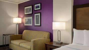 Una habitación de hotel con una cama, un sofá, dos lámparas y cuadros en la pared.