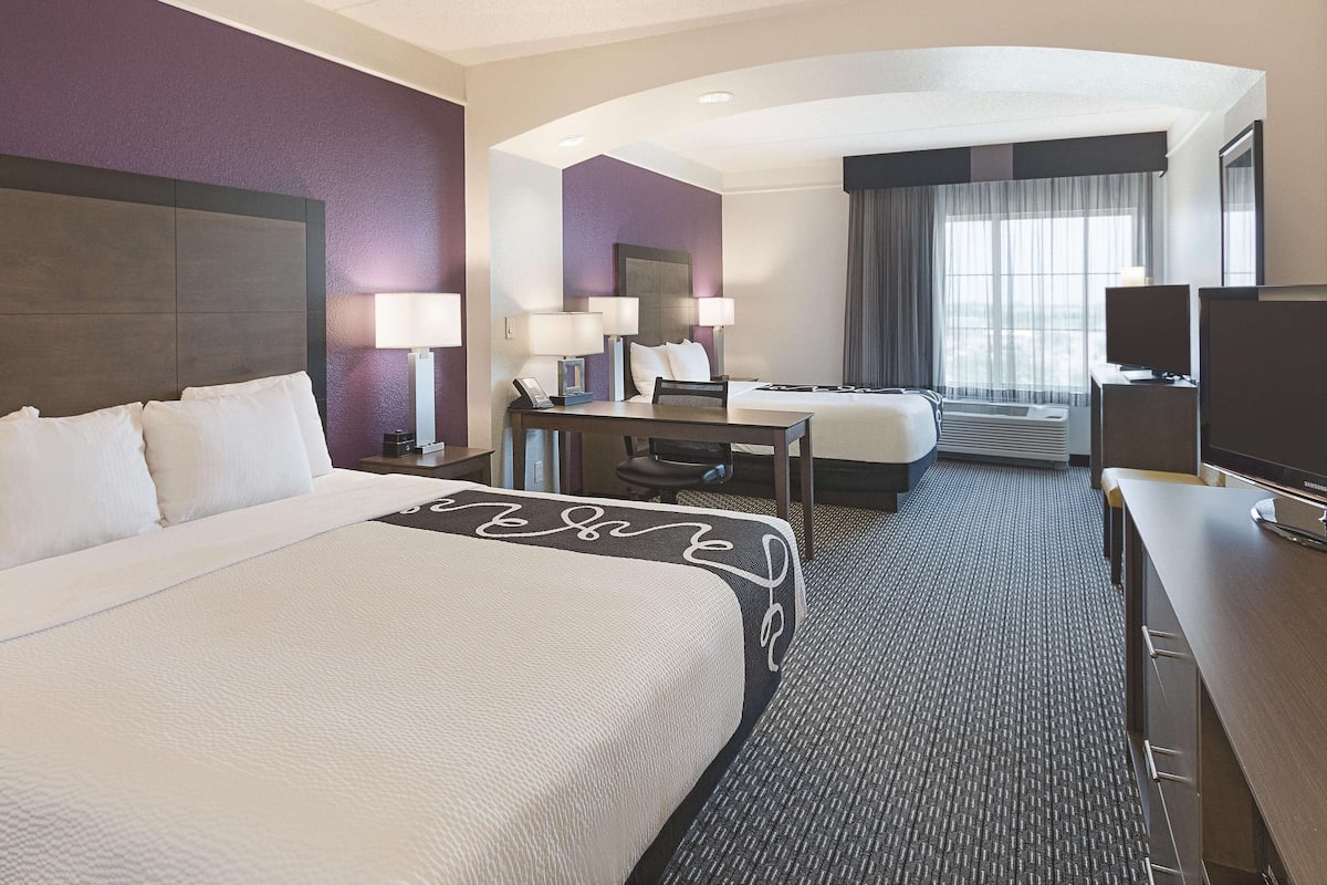 Habitación de hotel con una cama grande, un escritorio con una silla, un televisor y una ventana con cortinas.