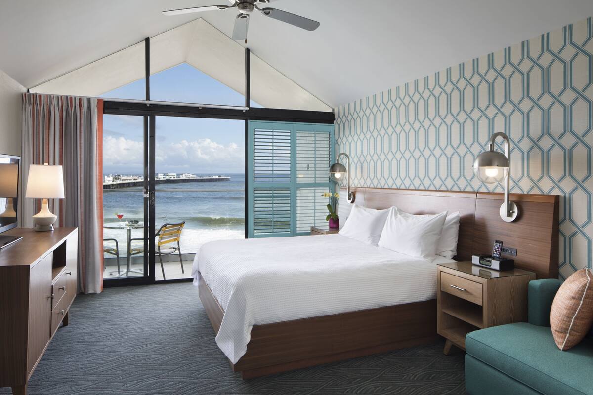 A hotel room with a large bed, a desk, a chair, a nightstand, and a view of the ocean.