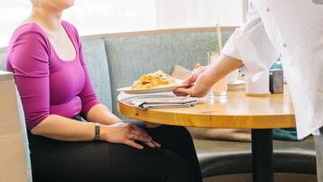 A person seated at a table with a plate of food, a drink, and a napkin.