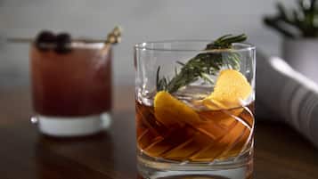 Two glasses of amber-colored beverages with lemon slices and rosemary, placed on a wooden surface.