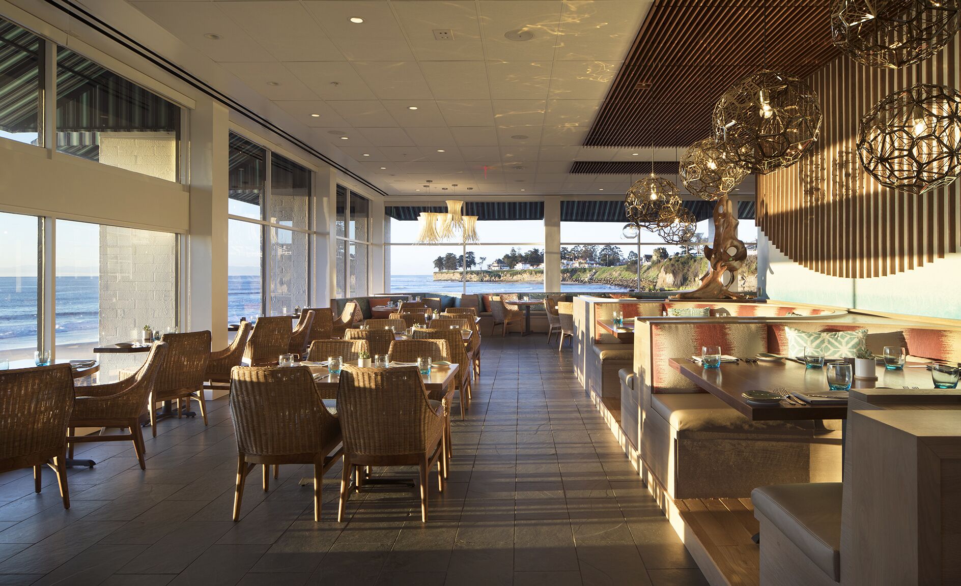 A restaurant with a view of the ocean, featuring wicker furniture and modern lighting.