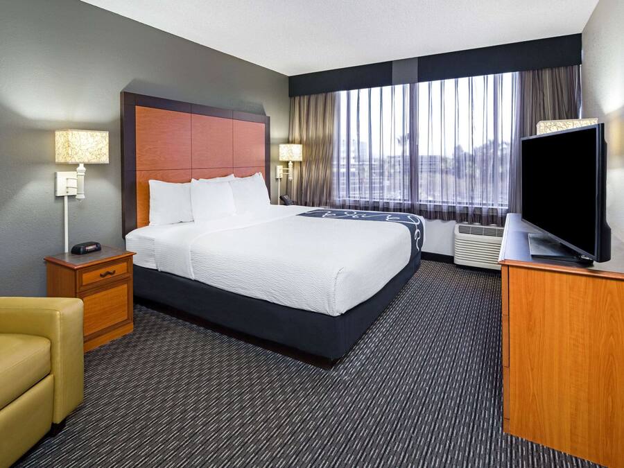 Une chambre d’hôtel avec un grand lit, un bureau doté d’un téléviseur à écran plat, une chaise, une table de chevet et une fenêtre avec des rideaux.