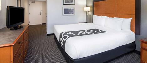 A hotel room with a large bed, a television, a dresser, and a carpeted floor.