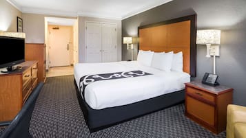 A hotel room with a large bed, a wooden dresser, a television, a bedside lamp, and a telephone on the nightstand.