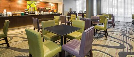 A hotel dining area with a buffet counter, multiple tables, and chairs.