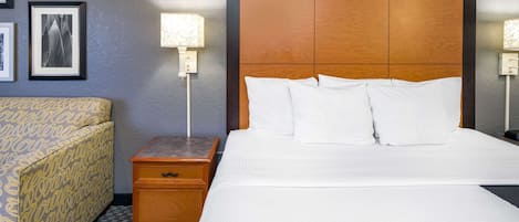 Habitación de hotel con una cama grande, una mesita de noche de madera, una mesita auxiliar y un sofá estampado.