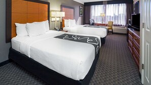 Una habitación de hotel con dos camas, un escritorio, una silla, un televisor y una ventana con cortinas.
