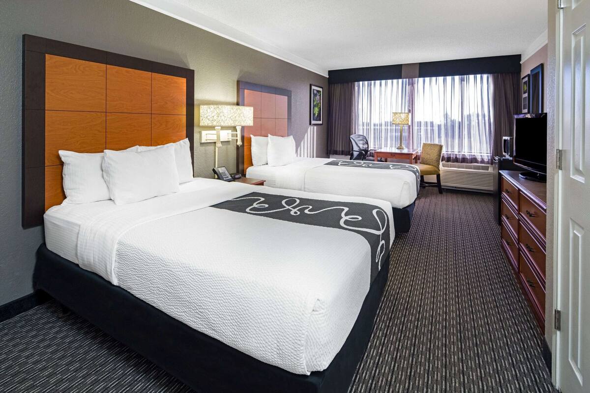 Una habitación de hotel con dos camas, un escritorio, una silla, un televisor y una ventana con cortinas.