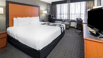 Een hotelkamer met een groot bed, een bureau met een flatscreen televisie, een stoel, een klein tafeltje en een raam met gordijnen.