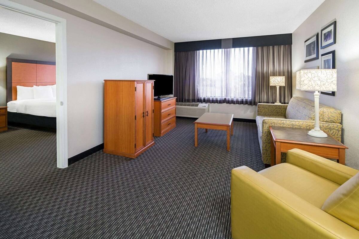 Habitación de hotel con cama, armario de madera, escritorio, sofá, lámpara y ventana con cortinas.