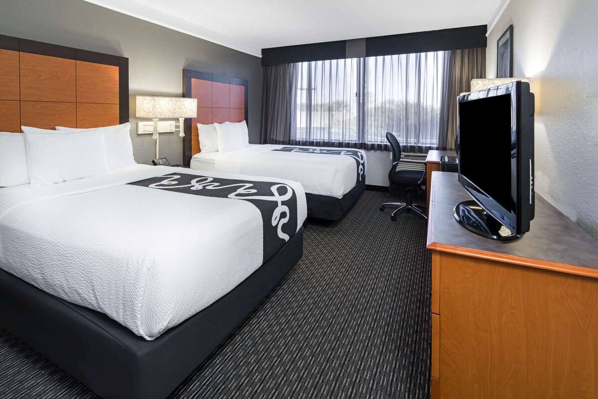 Habitación de hotel con dos camas, un escritorio, un televisor, una lámpara y una ventana con cortinas.
