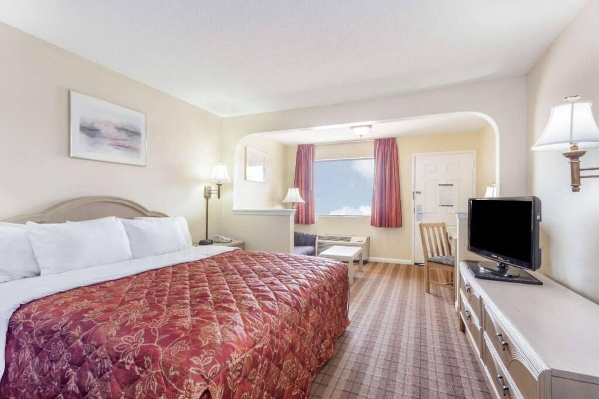 Habitación de hotel con cama, escritorio, silla, televisor y ventana con cortinas.