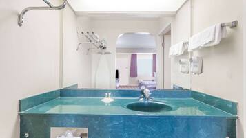 A bathroom with a large mirror, a glass sink, and a shower area.