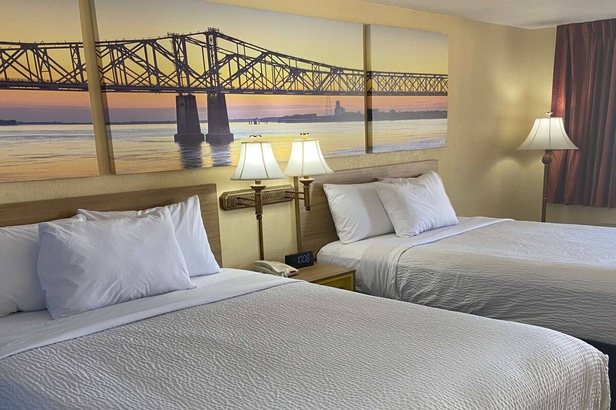 Habitación de hotel con dos camas, un cuadro de un puente, lámparas de noche y un reloj.
