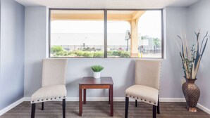 Ein Zimmer mit zwei Stühlen, einem kleinen Tisch und einem großen Fenster mit Blick auf ein Gebäude und Grünflächen.