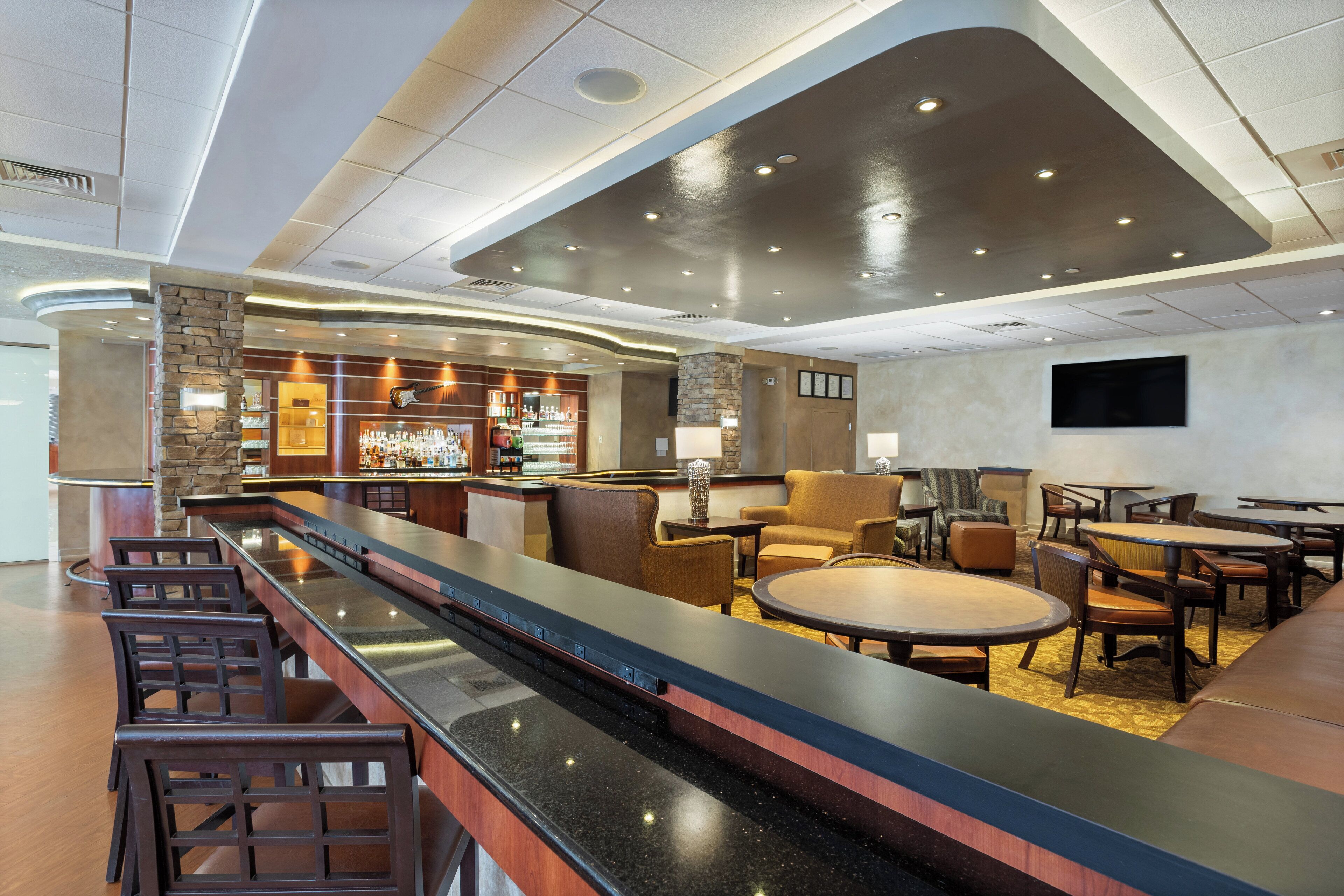 A modern bar area with a long counter, multiple seating options, and a well-lit ceiling.