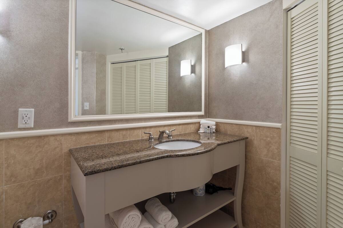 A bathroom with a granite countertop sink, a large mirror, and a towel rack.
