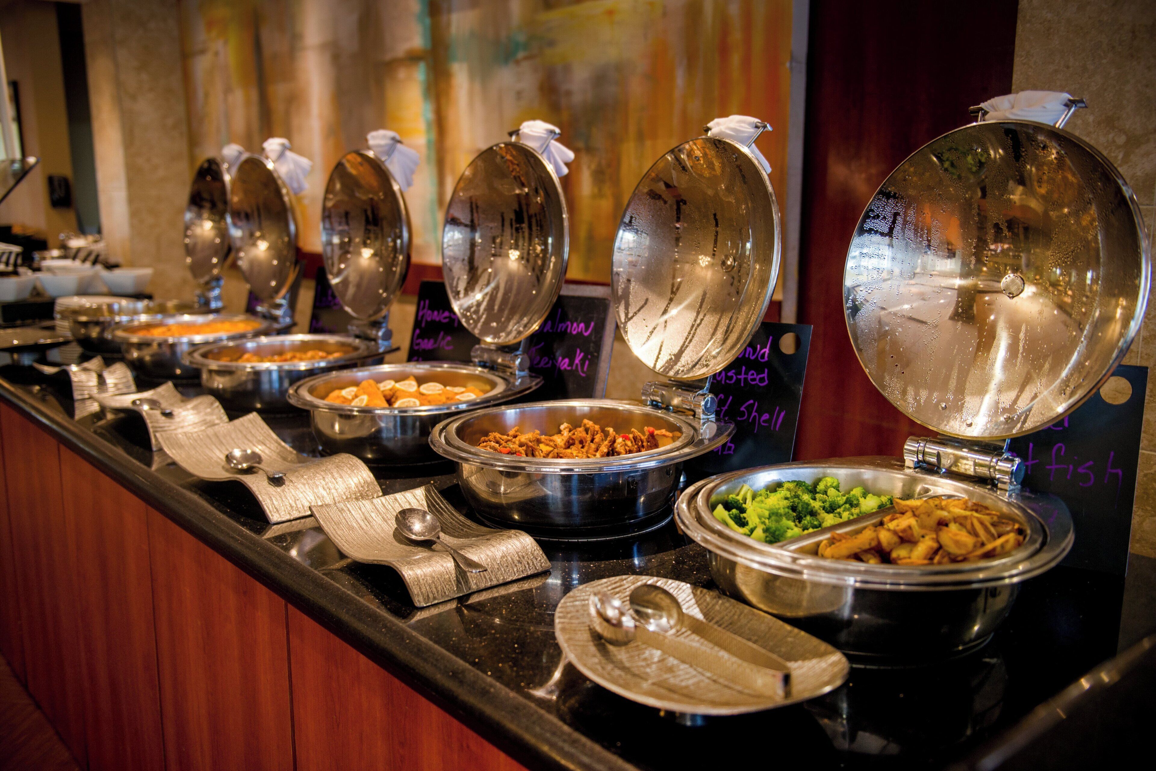 A buffet line with various food dishes and utensils.