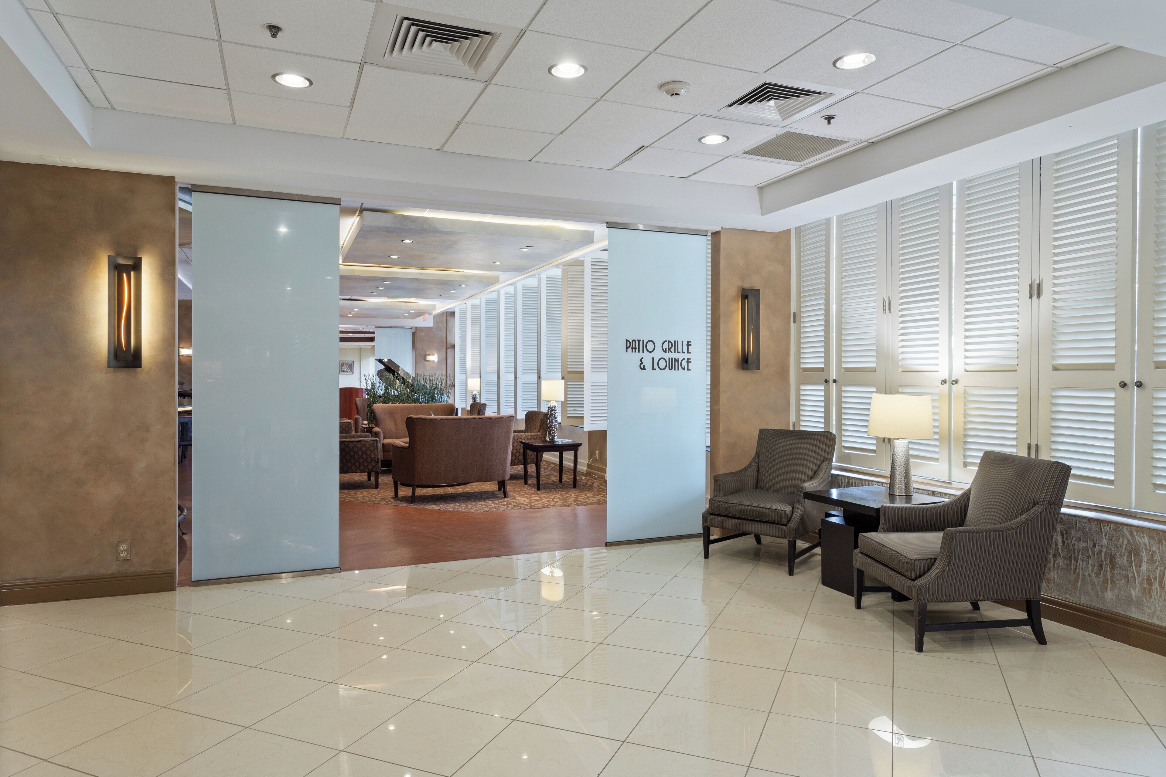 A lobby with a tiled floor, seating area with chairs and a table, and a sign reading "Patio Grille & Lounge".