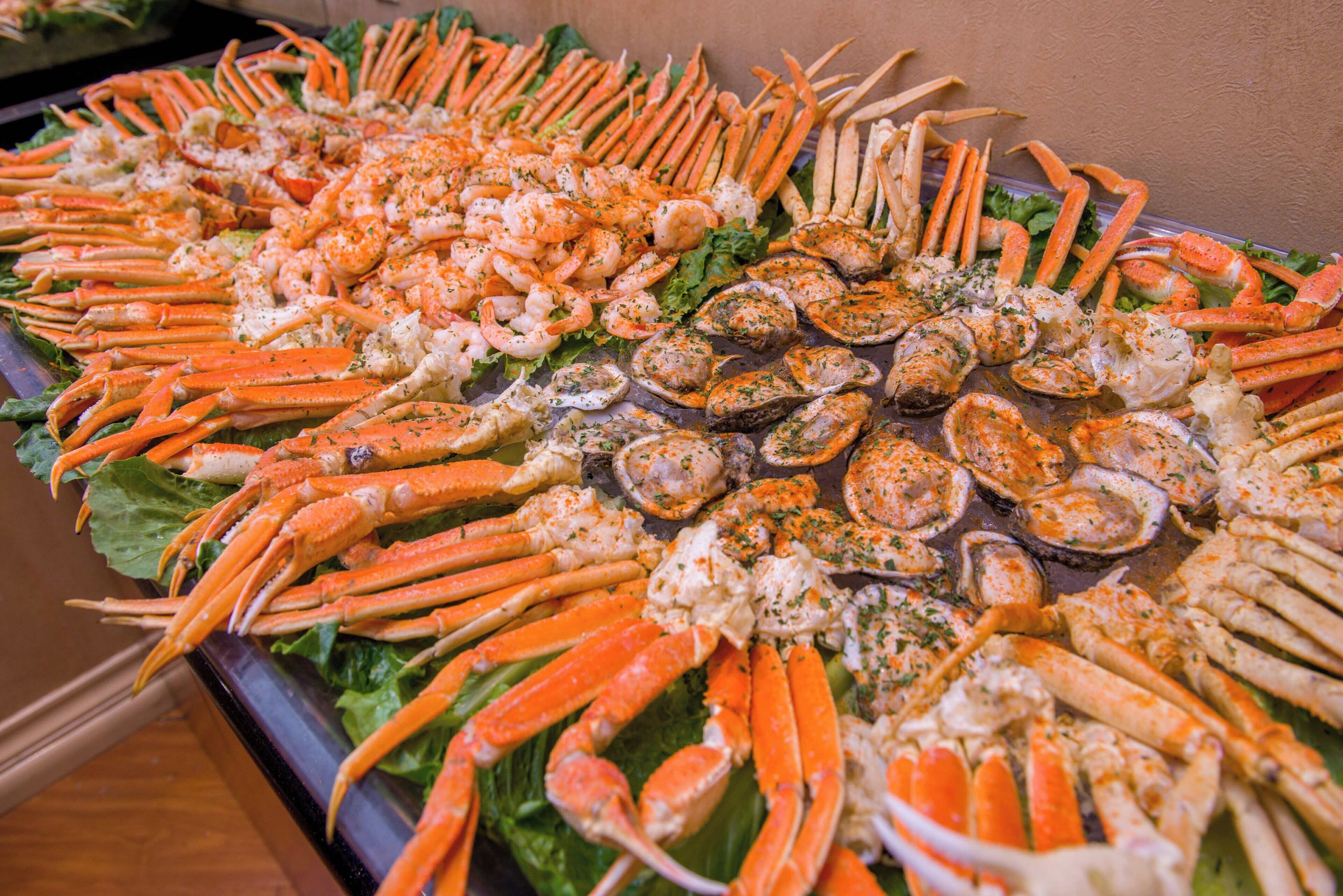 A buffet table with various seafood items, including crab legs and oysters, arranged on a bed of lettuce.