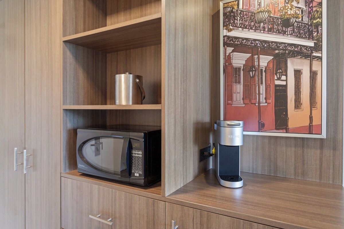 Uma cozinha compacta com micro-ondas, cafeteira e uma prateleira com panela de aço inoxidável.