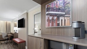A hotel room with a kitchenette, a flat-screen TV, a coffee machine, a microwave, a bench, and a painting of a building. - Crowne Plaza Executive Center Baton Rouge by IHG (Baton Rouge)