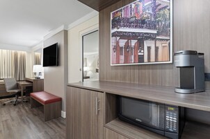 Habitación de hotel con kitchenette, televisión de pantalla plana, cafetera, microondas, banco y un cuadro de un edificio.