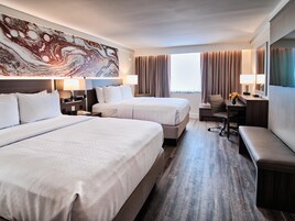 Habitación de hotel con dos camas, un escritorio, una silla y un cuadro abstracto grande en la pared.