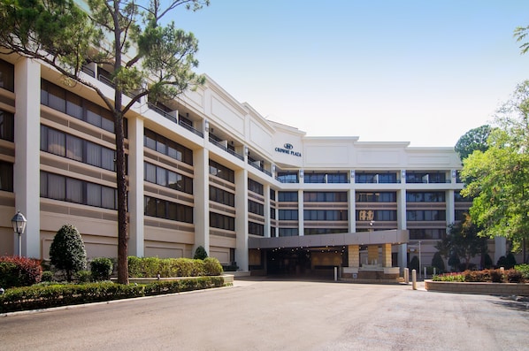 A multi-story hotel with a central entrance, balconies, and a landscaped driveway.