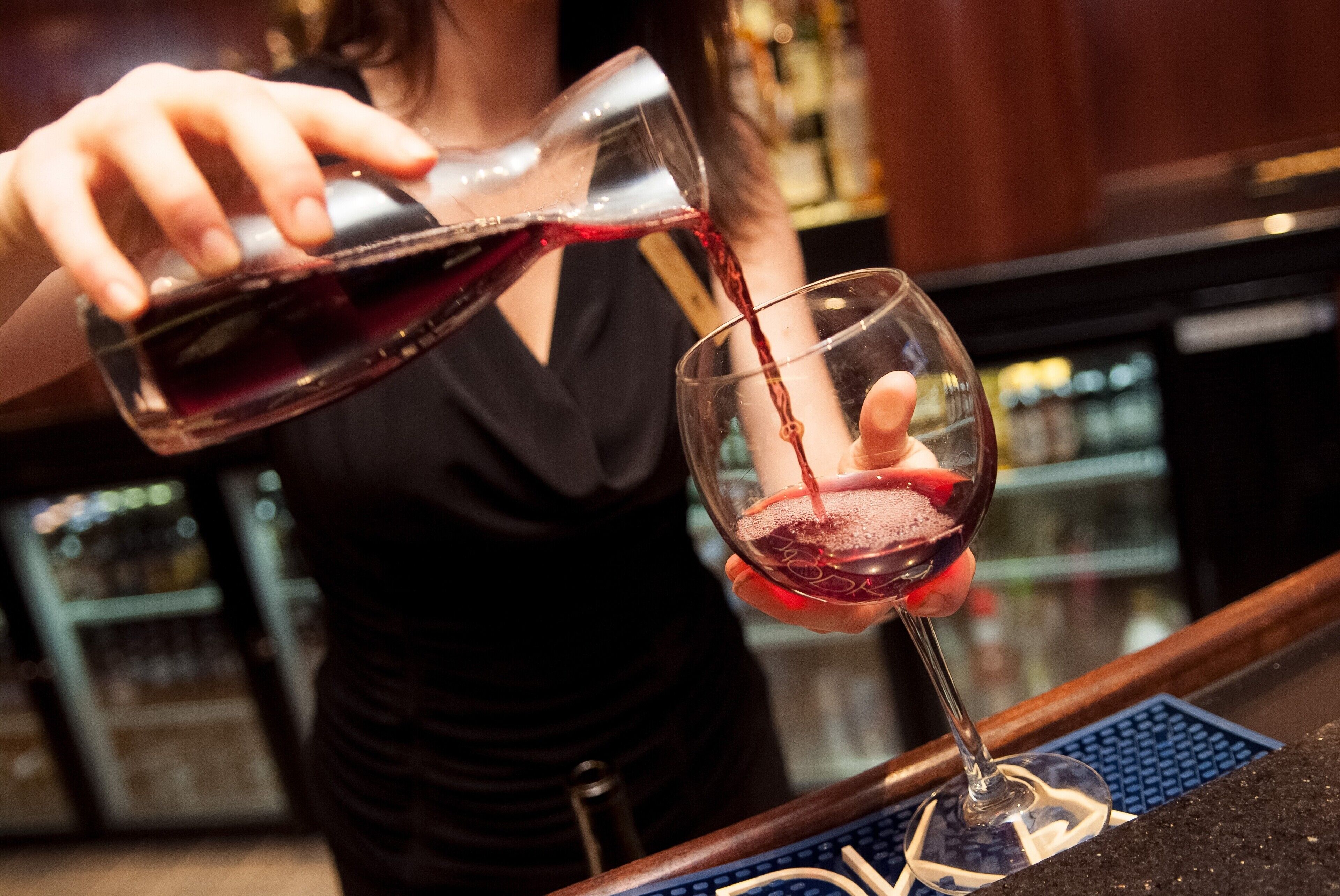 A person pouring red wine into a glass.