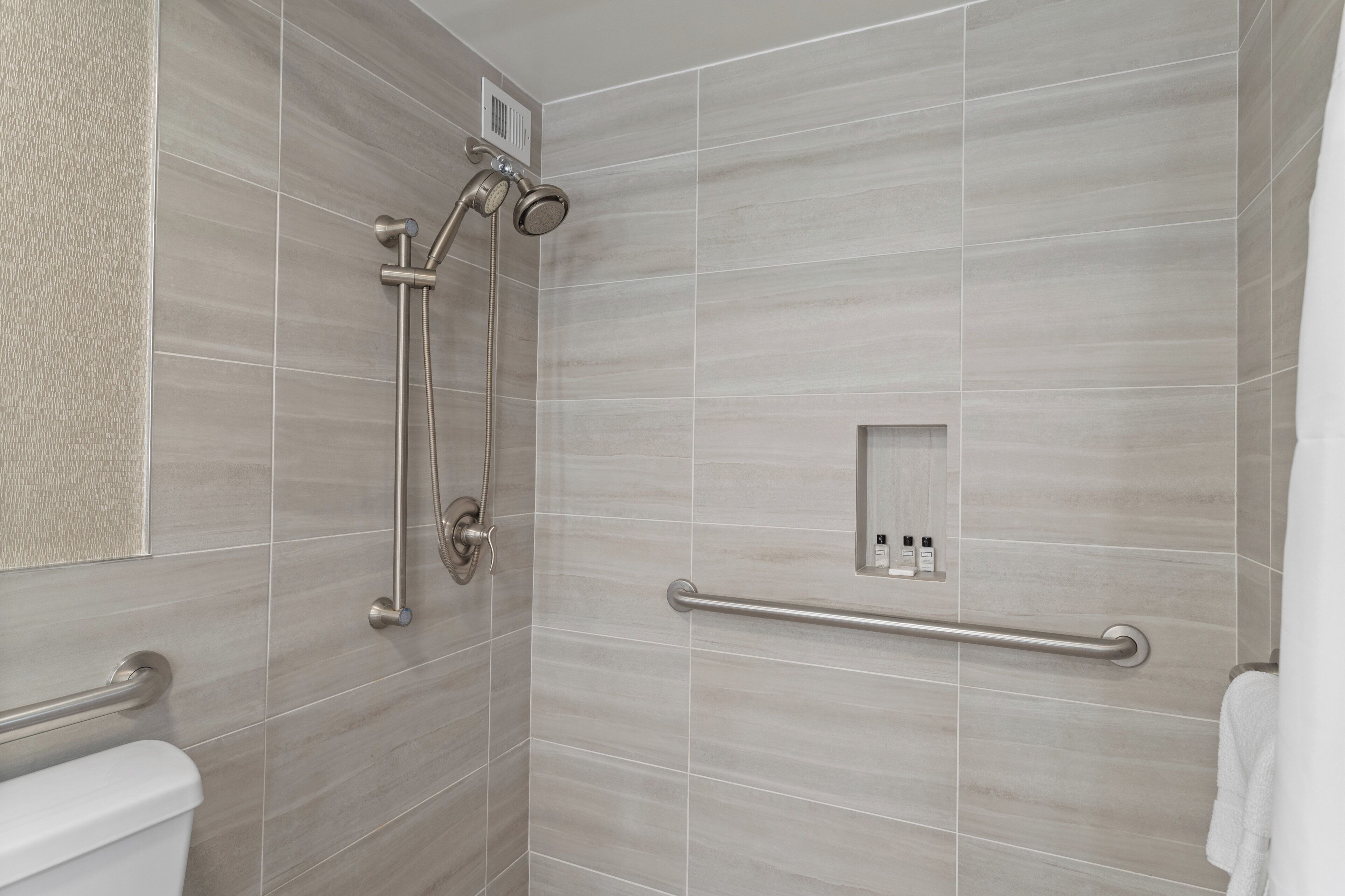 A modern bathroom with a shower, grab bar, and toilet.