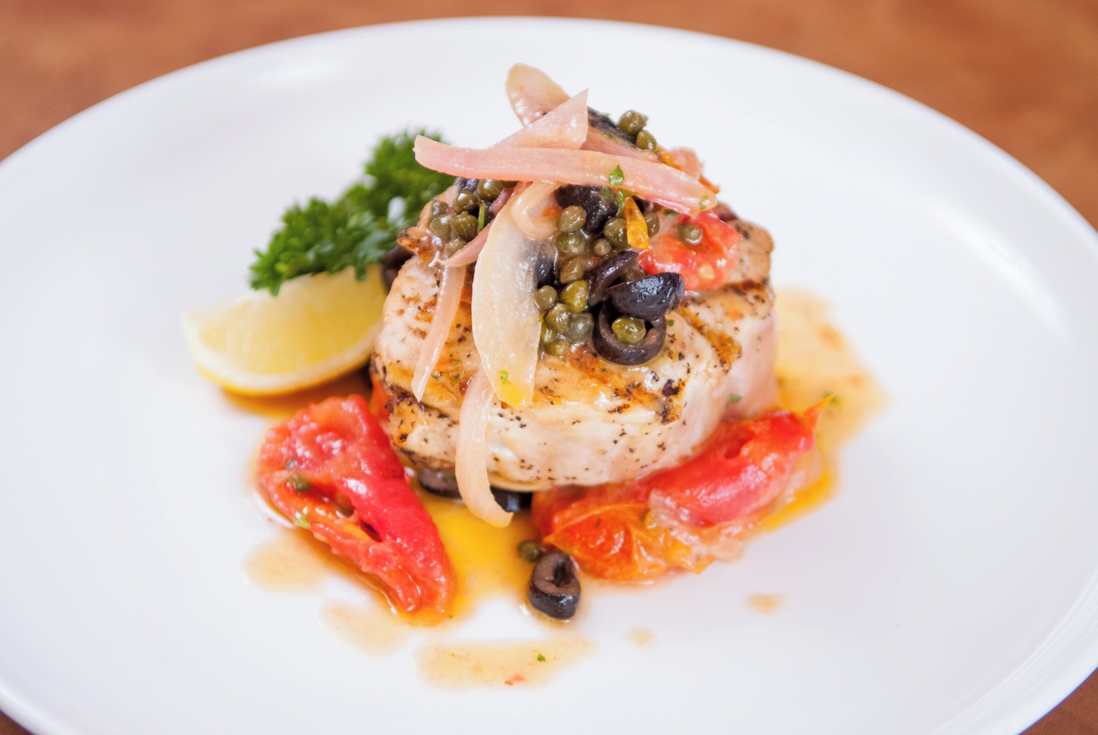 Un plato blanco con un guiso de pescado, limón y alcaparras.