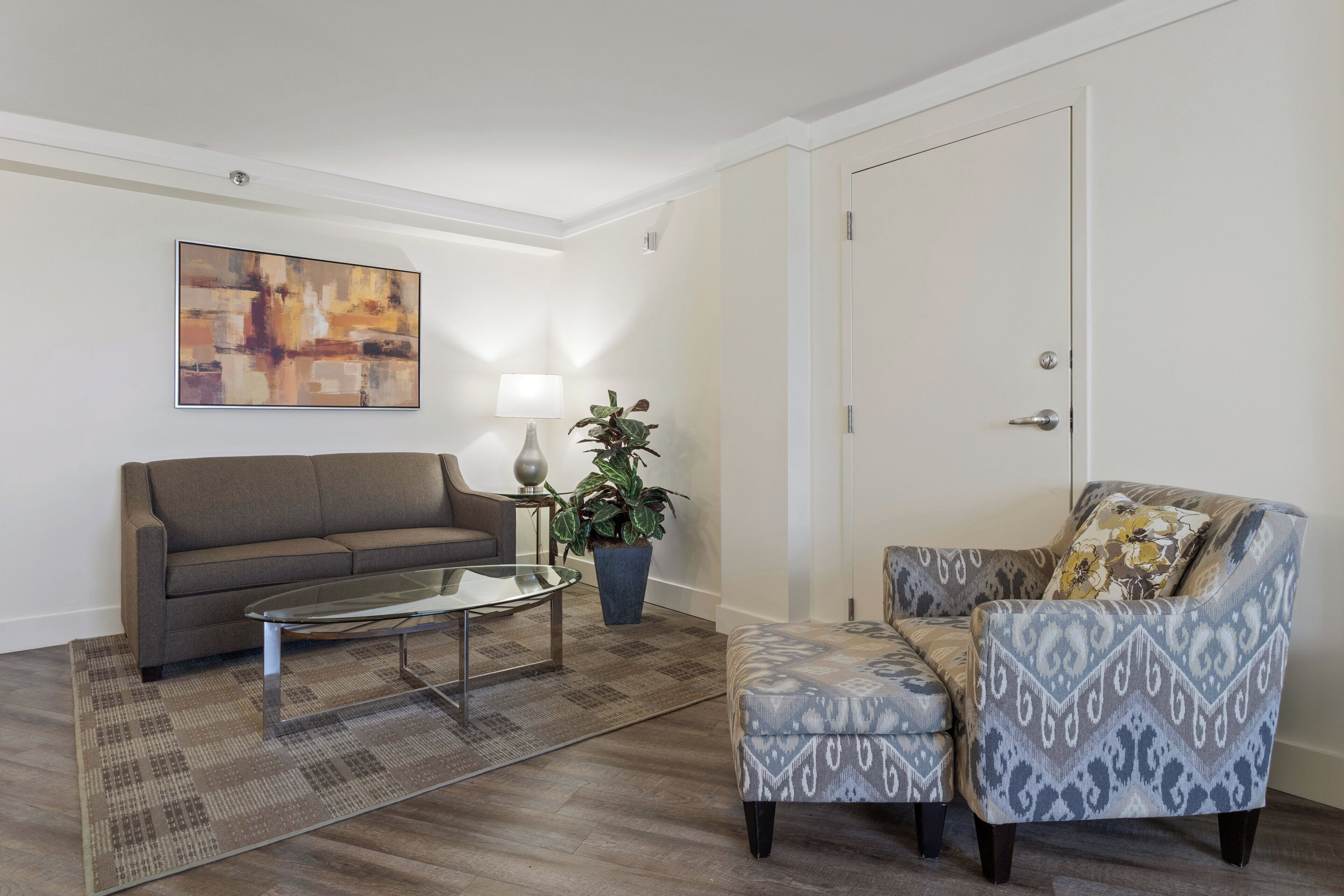 A living room with a sofa, armchair, coffee table, lamp, and a painting on the wall.