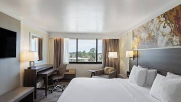 A hotel room with a large bed, a desk, a chair, a TV, and a window with curtains.