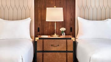 A hotel room with two beds, a wooden headboard, a bedside table with a lamp, and a small vase with flowers.