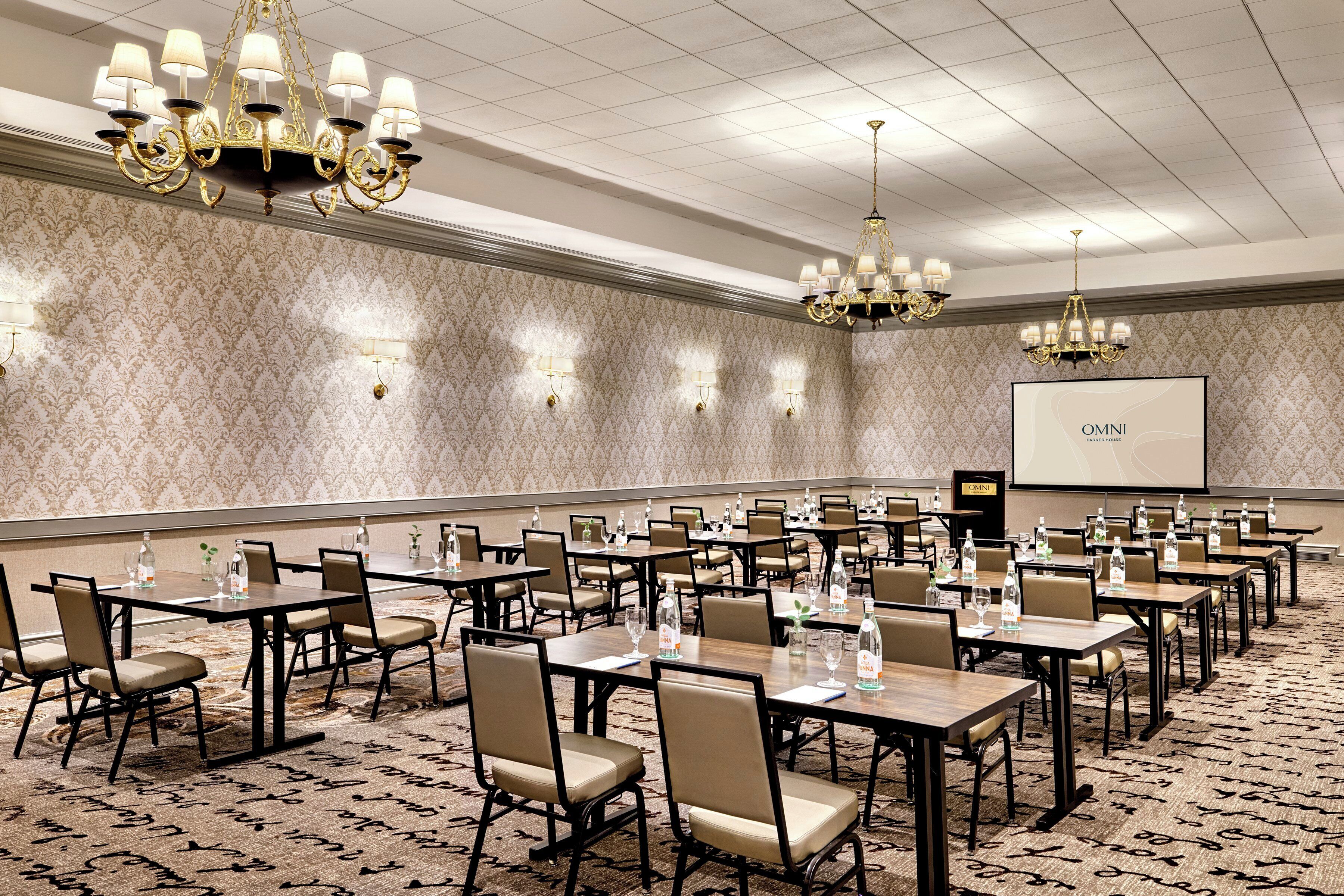 Un salón de conferencias con varias mesas y sillas, equipado con botellas de agua y vasos, y una pantalla de proyector que muestra 'OMNI PARKER HOUSE'.